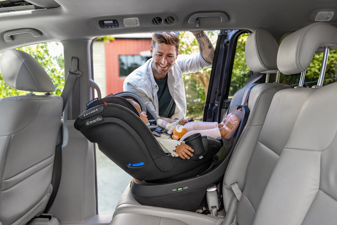 Man looks on at child in Revolve360 Slim 2-in-1 Rotational Convertible Car Seat in rear-facing mode